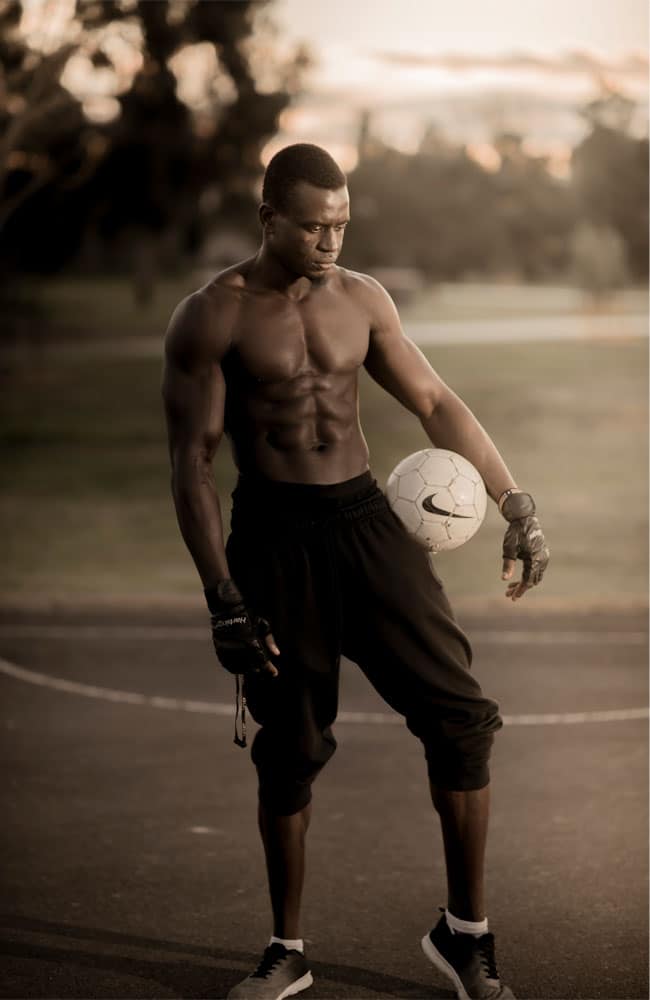 Professional portrait of a shirtless man posing with soccer ball